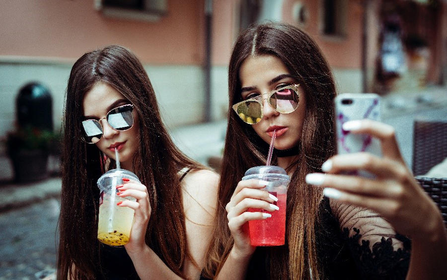 Two girls drinking beverages, one of them taking a selfie